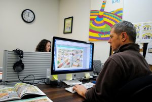 Publications Director Bob Rugh edits pages that will be featured in The Language Conservancy’s printed booklets. Graphic designer Allison Horner works in the background. | Photo by Nicole McPheeters