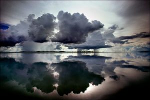 Menacing cumulus clouds are mirrored in the placid waters of Lake Murray, the largest lake in Papua New Guinea, covering an area of some seven hundred square miles. About five thousand indigenous inhabit this lake region. in 1923, "The New York Times" reported on an Australian expedition that used amphibious airplanes to chart Lake Murray and the explorers' close encounters with indigenous people called, at the time, "head-hunters." | © Steve Raymer / National Geographic Creative