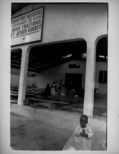 Les Fantômes de N’Zao (The Ghosts of N’Zao), N’Zao, Guinea, 2009, Gelatin Silver Print. Young boy stands outside of Hope Medical Clinic.