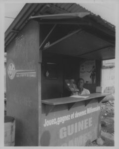 Guinee Games, Conakry, Guinea, 2009, Gelatin Silver Print. Man sells lottery tickets out of a corrugated tin shack.